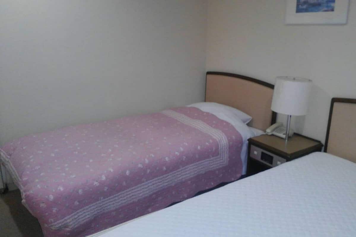 A single bed with a white mattress and a pink blanket with a floral pattern.
