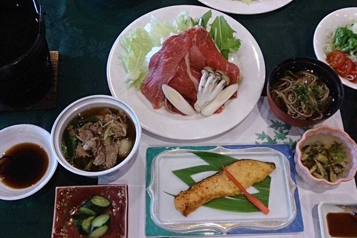 A table with various dishes including meat, vegetables, and a bowl of soup.