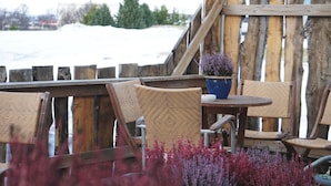 A wooden deck with wicker chairs and a round table, overlooking a snowy landscape. - Tehúsið Hostel (Egilsstaðir)
