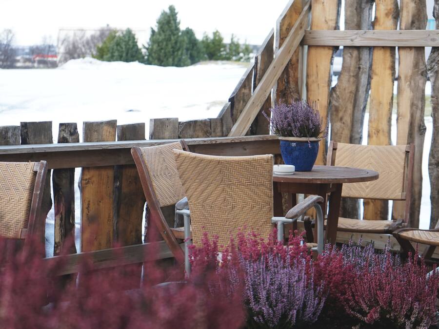 A wooden deck with wicker chairs and a round table, overlooking a snowy landscape.