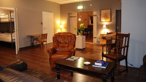 A living room with a sofa, a coffee table with books, a leather armchair, and a dining area with a table and chairs. - Tehúsið Hostel (Egilsstaðir)