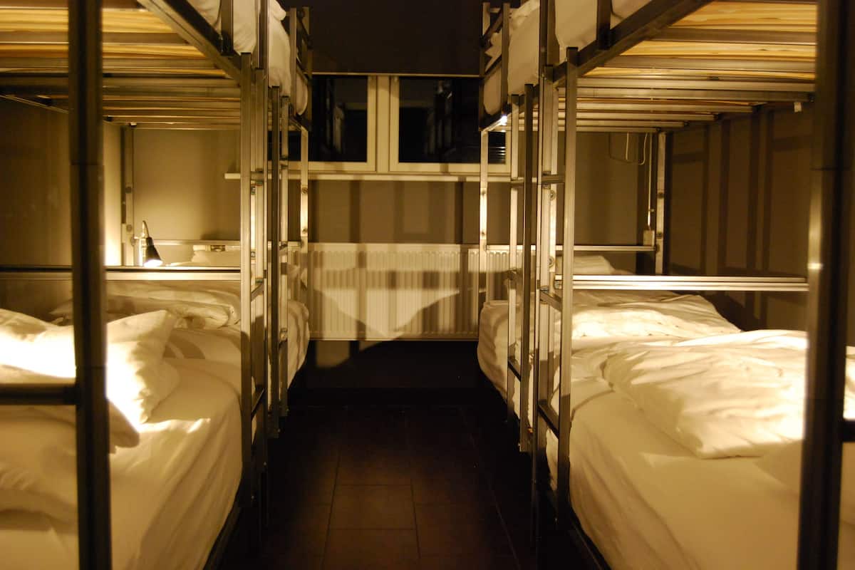 A narrow corridor with bunk beds on either side, a radiator in the center, and a window at the far end.