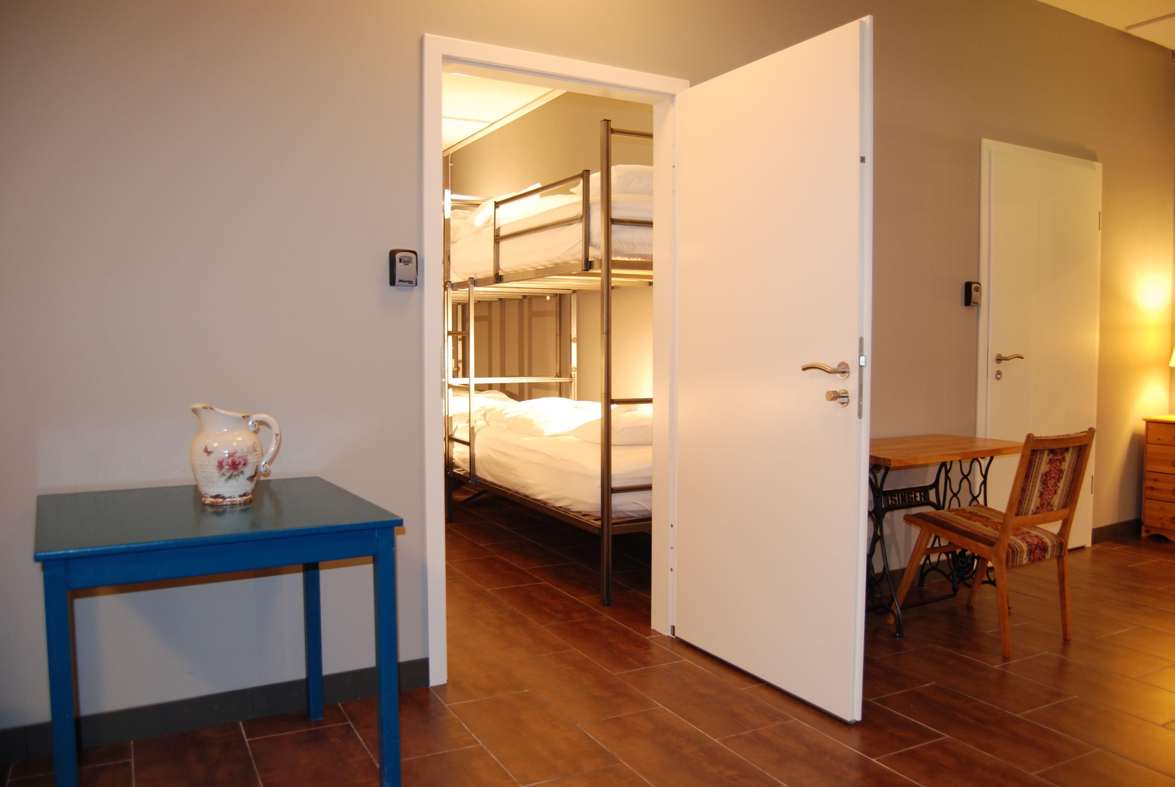 Una habitación con literas, una mesa con jarrón y una silla.