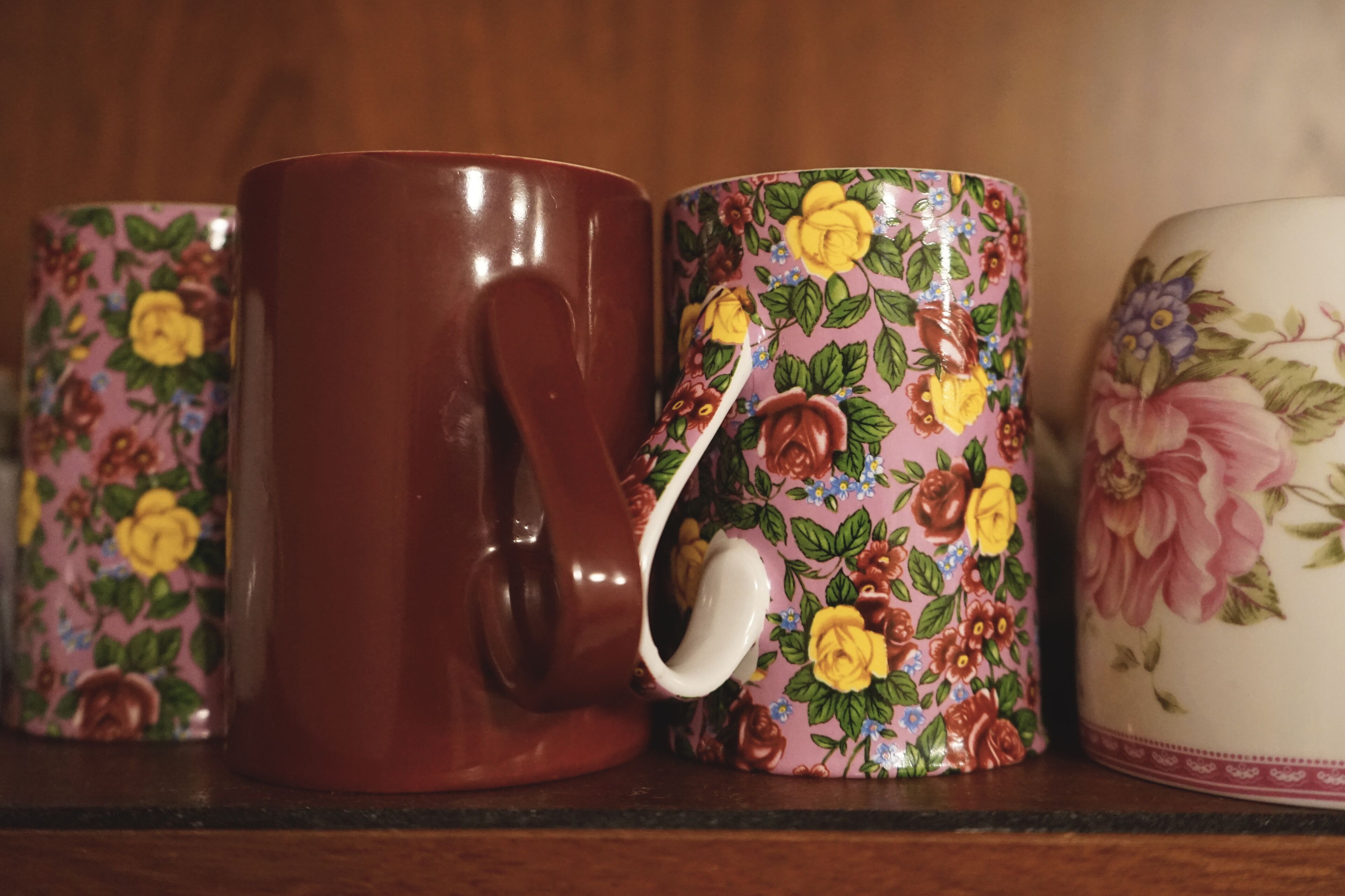 Une rangée de tasses en céramique ornées de motifs floraux, posées sur une étagère.