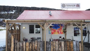 A rustic building with a red roof, wooden walls, and a sign advertising a cafe, bar, and hostel. - Tehúsið Hostel (Egilsstaðir)