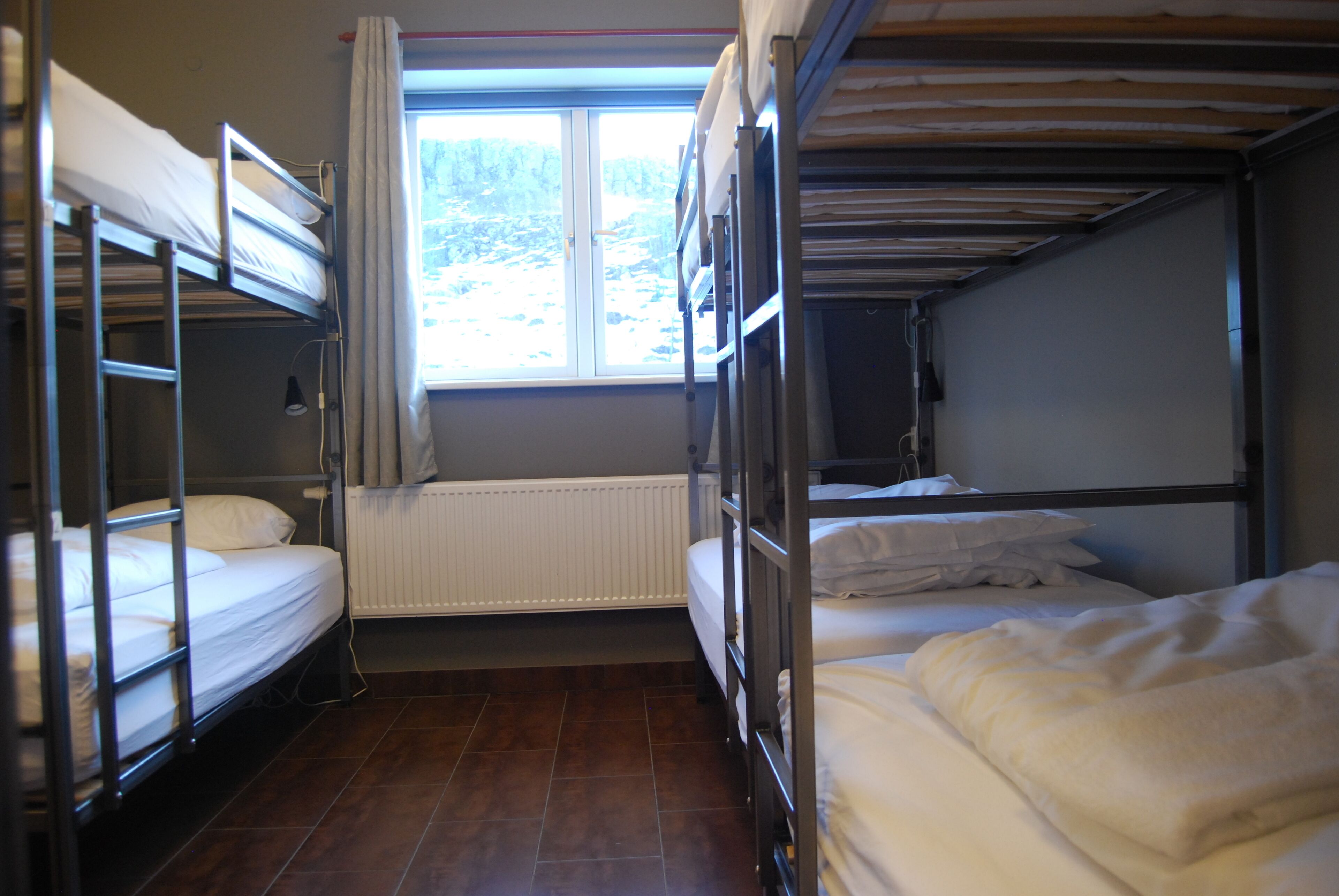 A bunk bed room with a window, a radiator, and a wooden floor.