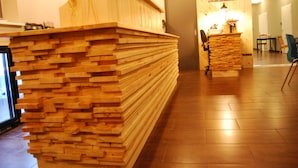 A reception desk made of stacked wooden planks, a clock, and a small desk with a lamp. - Tehúsið Hostel (Egilsstaðir)