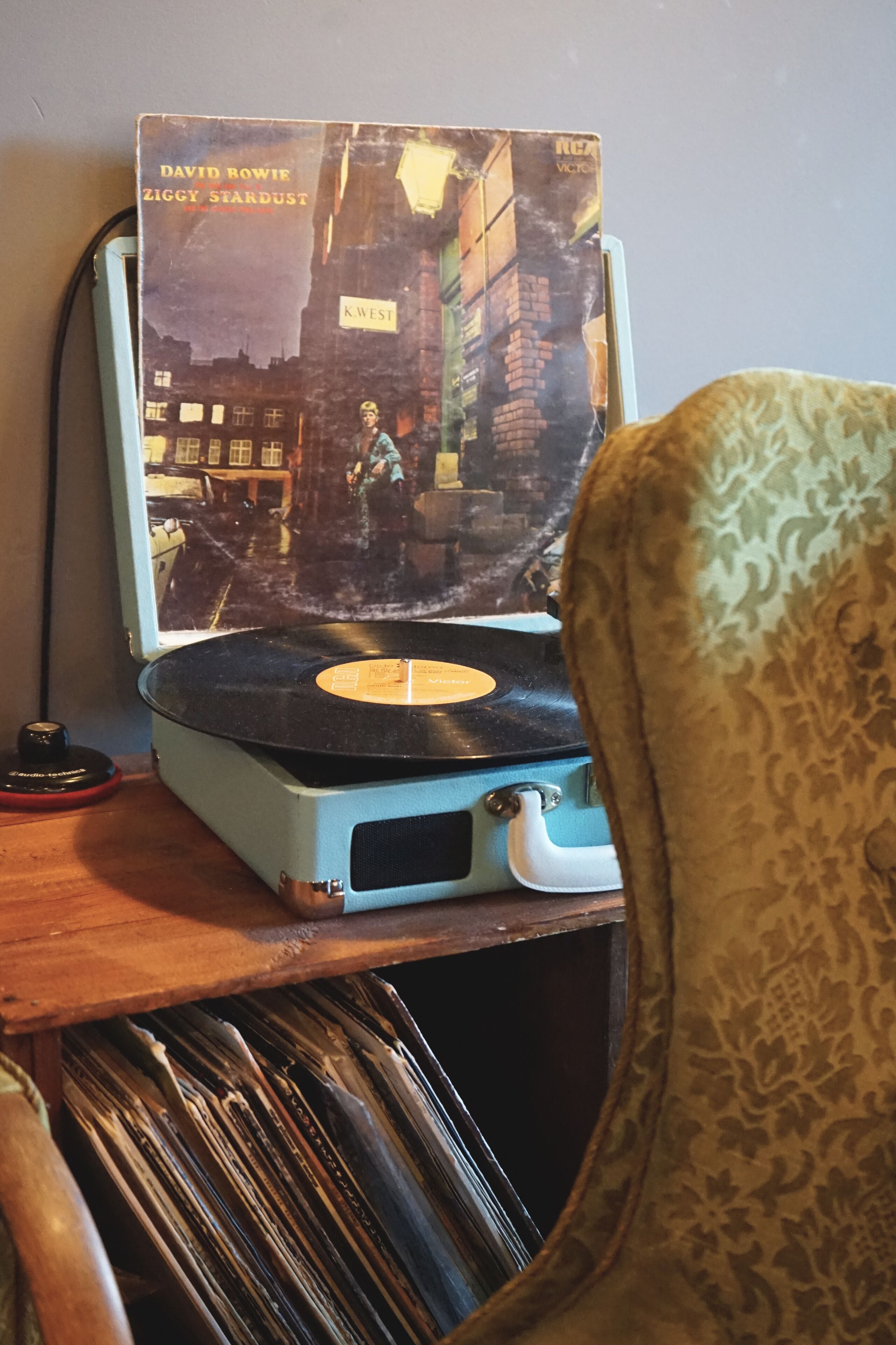 A turntable with a vinyl record and a book titled "David Bowie Ziggy Stardust" on a wooden surface.