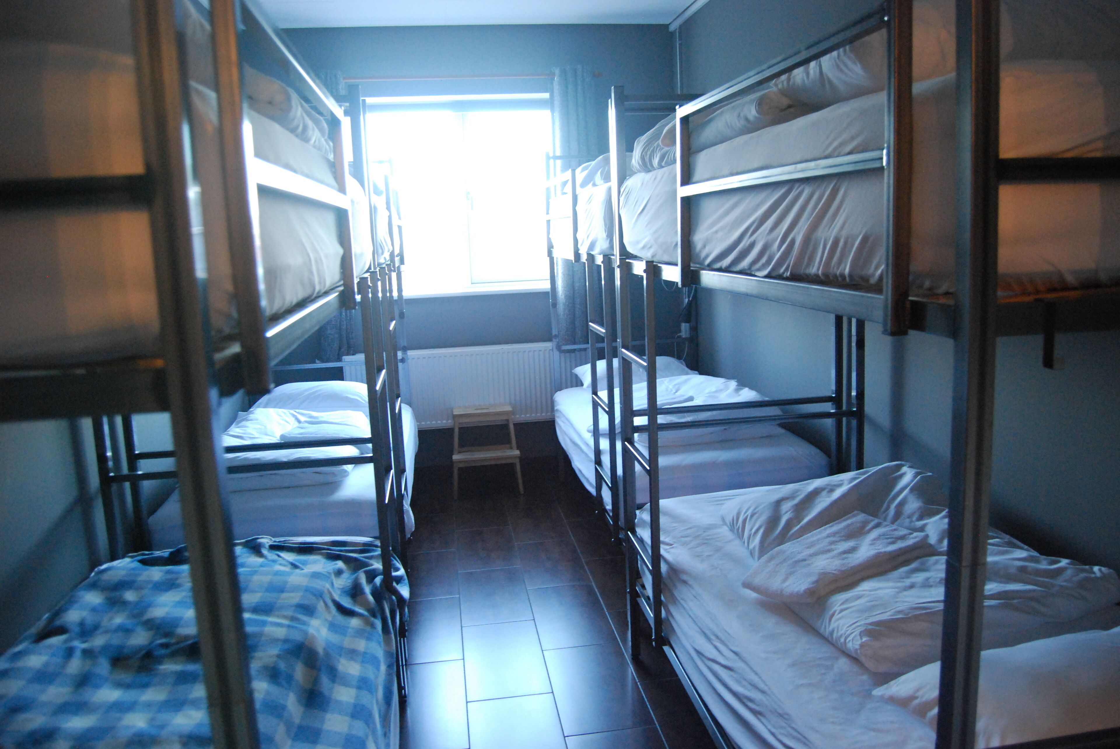 A dormitory room with bunk beds, a small table, and a window providing natural light.