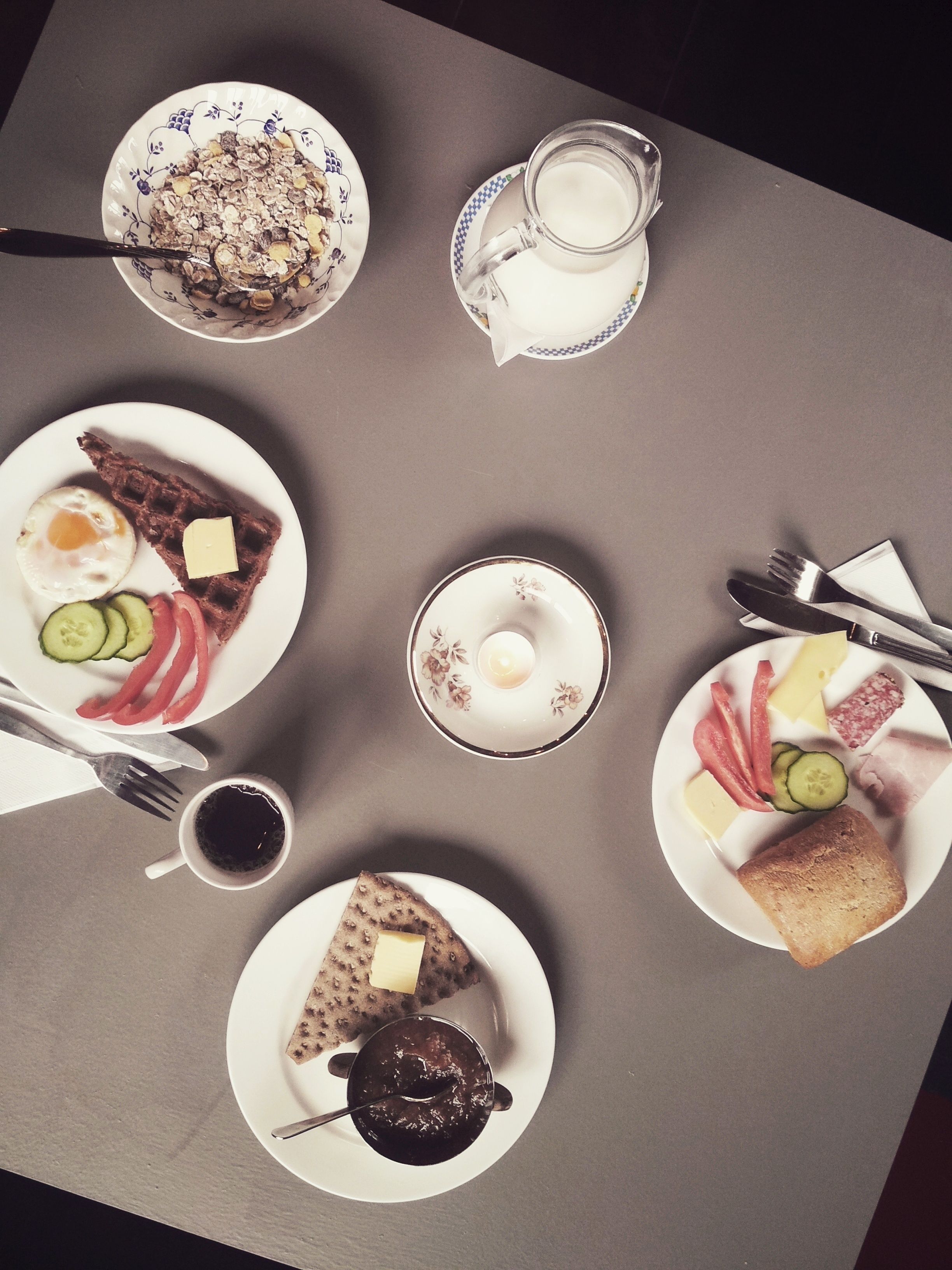 Ein Tisch reichhaltig mit Frühstücksartikeln gedeckt, darunter Müsli, Waffeln, Eier und Toast.