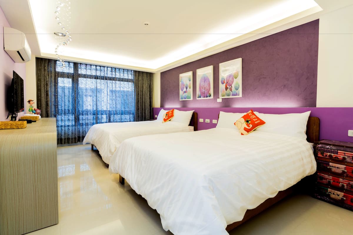 A hotel room with two beds, a desk, and a large window with curtains.
