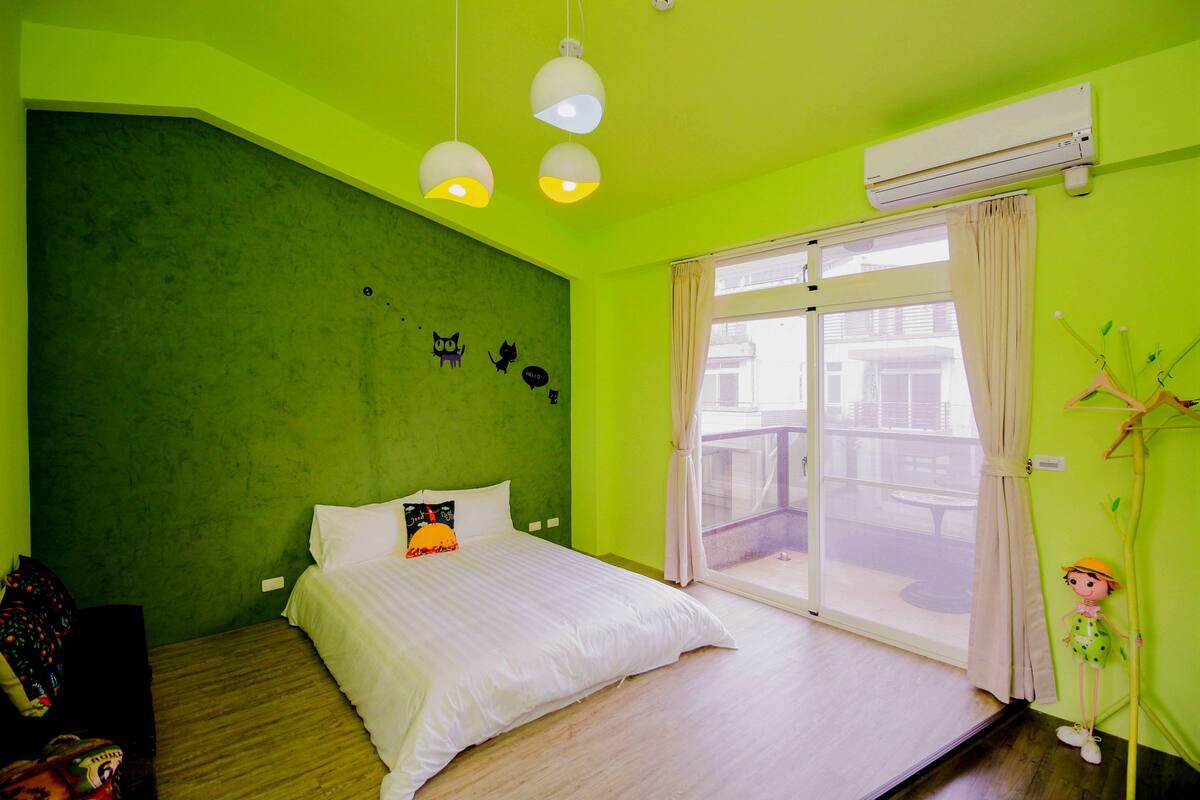 A bright green room with a bed, a window with a view, and a hanging plant.