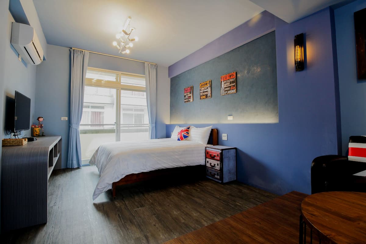 A hotel room with a bed, a desk, a chair, a TV, and a window with curtains.