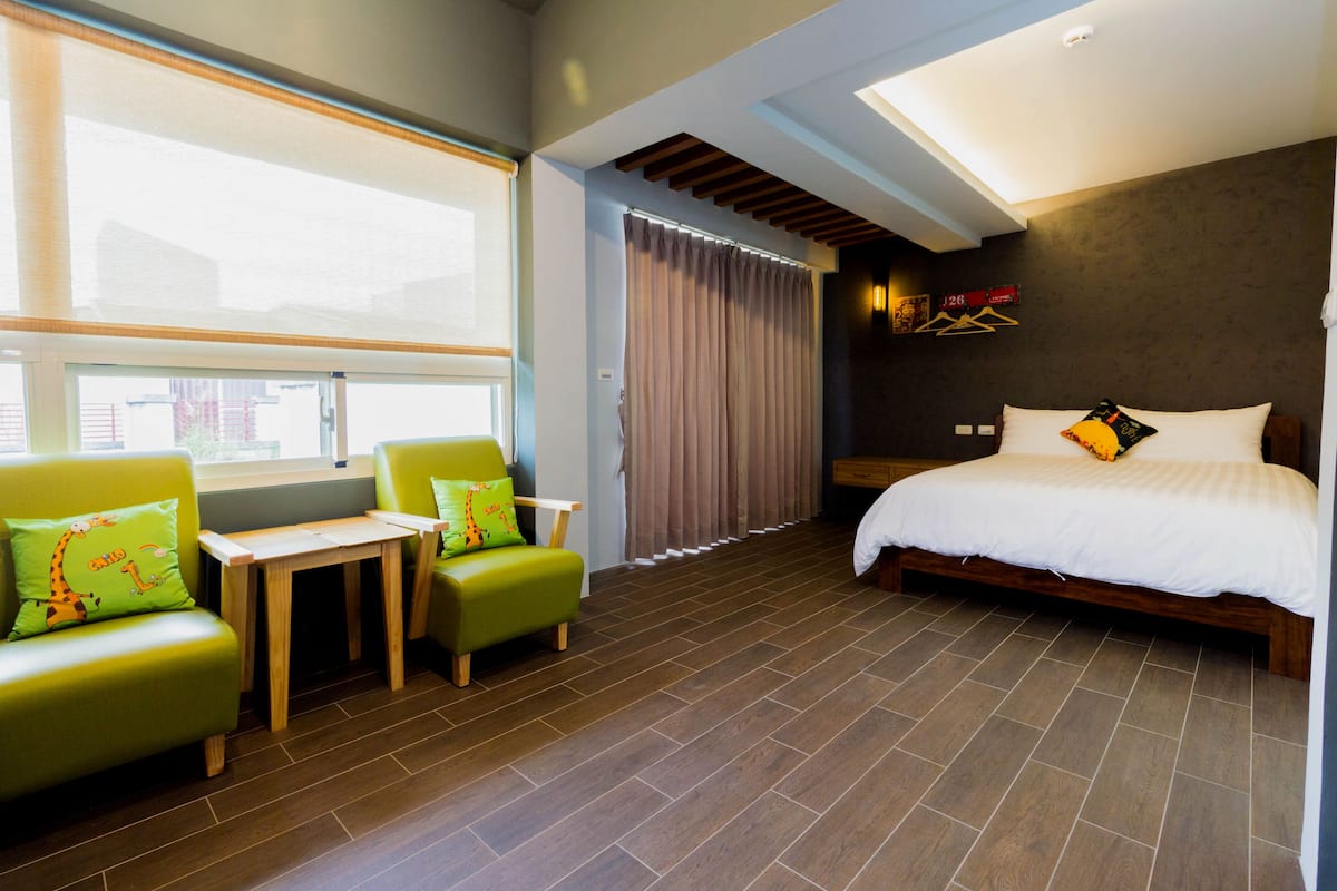 A hotel room with a bed, a small table, two chairs, and a window with curtains.