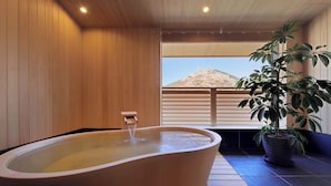 Une salle de spa dotée d’une baignoire sur pieds, de murs en bois, d’une grande fenêtre offrant une vue sur la montagne et d’une plante en pot.