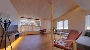 Un salon spacieux avec un plafond haut, un canapé, un fauteuil en cuir, une lampe sur pied et une vue sur les cerisiers en fleurs, visible à travers une grande fenêtre.