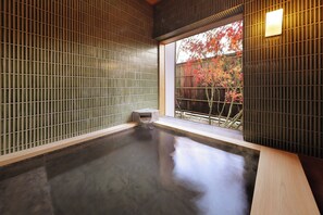 Ein traditionelles japanisches Onsen mit einer Holzbank und Blick auf Herbstlaub durch ein Fenster.