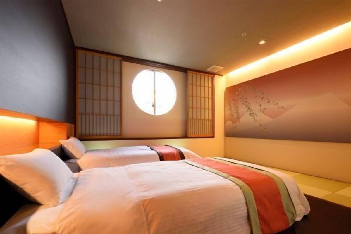 Une chambre d’hôtel avec deux lits, une grande fenêtre et une porte coulissante de style japonais traditionnel.