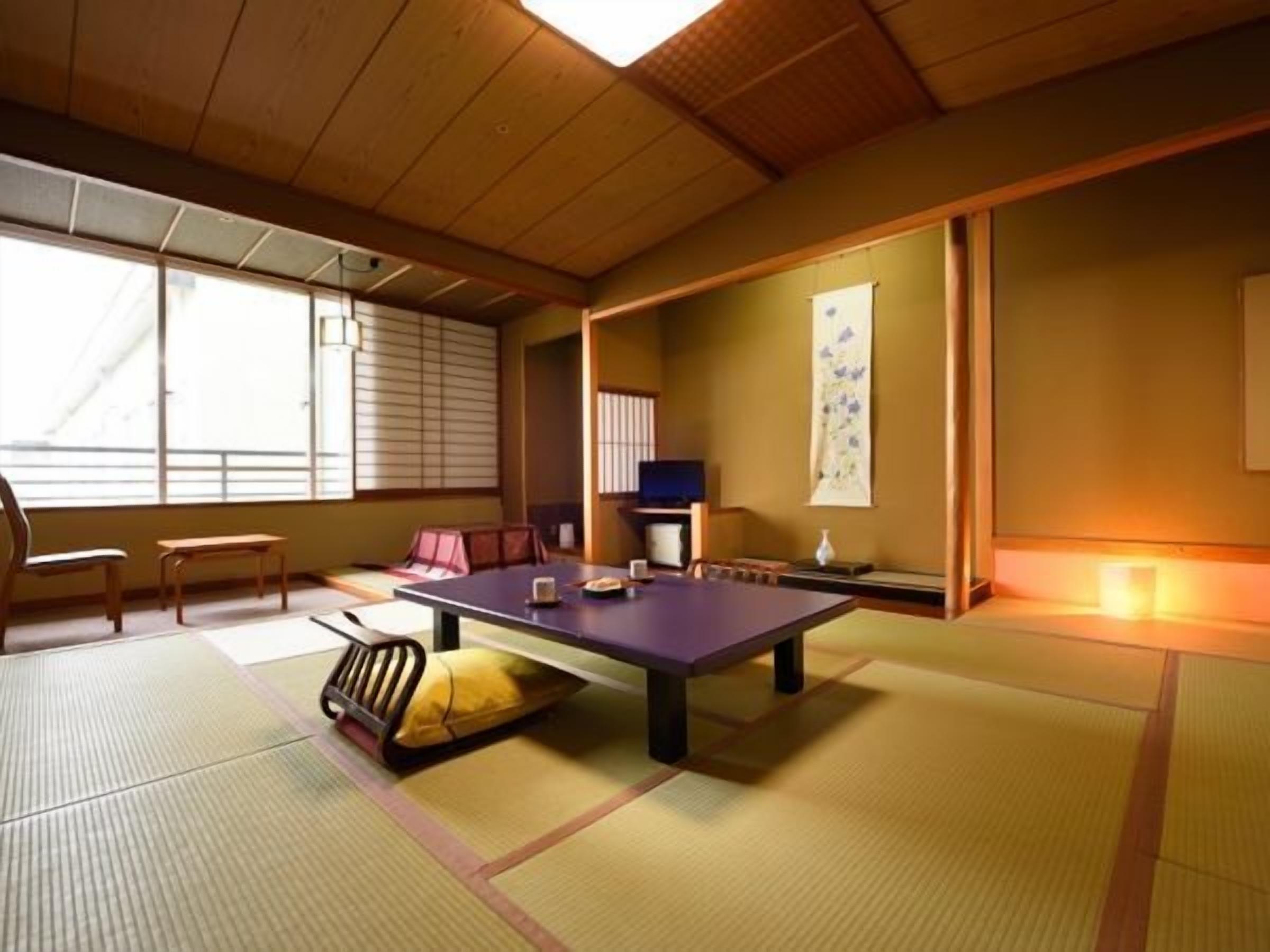 A tatami mat room with a low table, chairs, a television, and a sliding door.