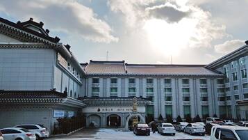 A hotel with a traditional architectural style, featuring a central entrance with a fountain, surrounded by parked cars.