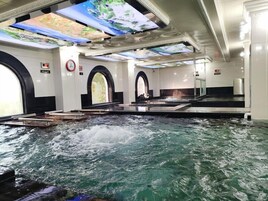 Ein Thermalbereich mit großem Innenpool, mehreren Panoramafenstern und einer digitalen Anzeige an der Decke.