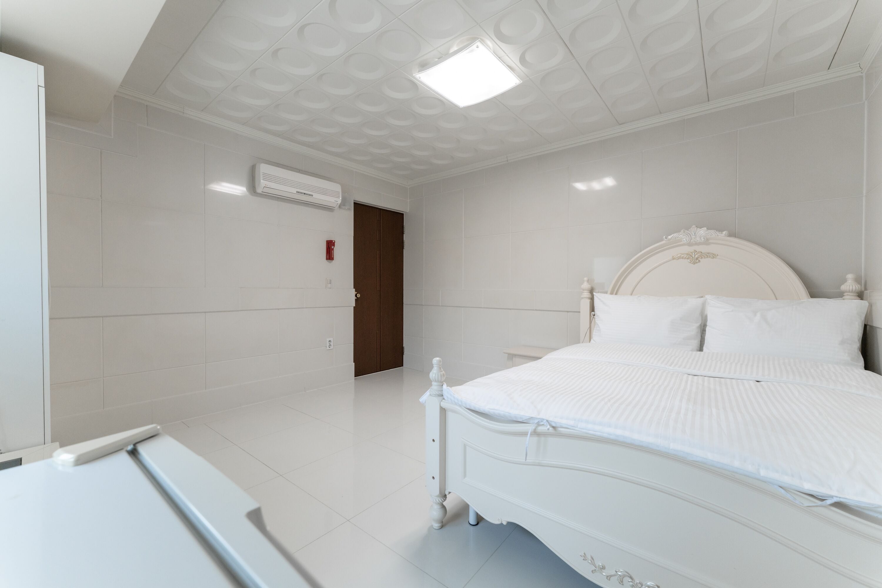 A bedroom with a white bed, white walls, and a white ceiling with a recessed light.