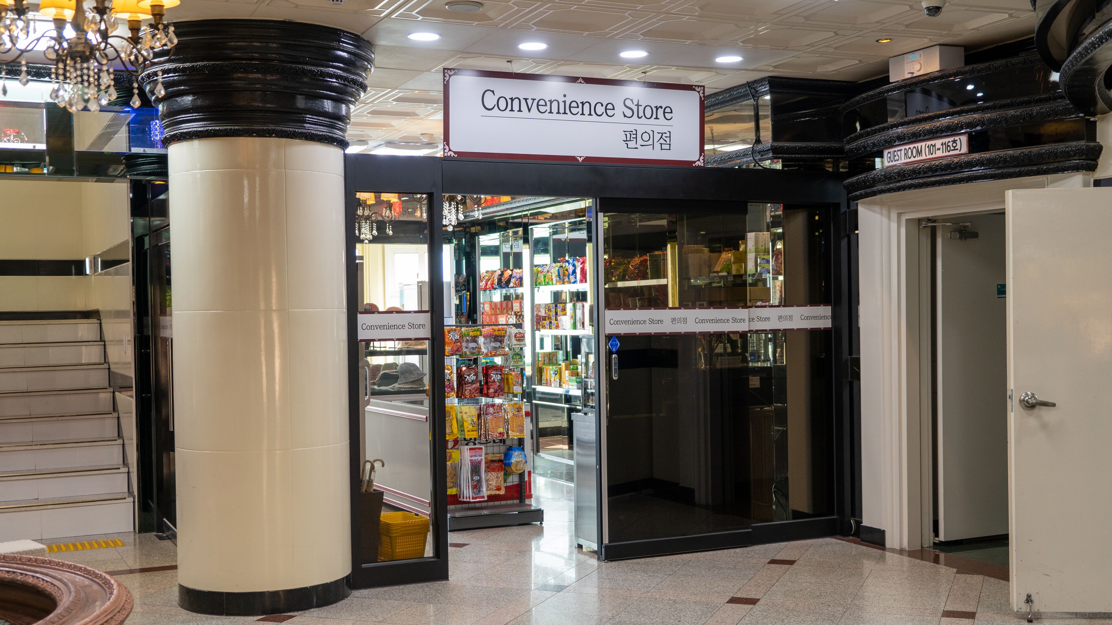 Ein Convenience Store mit einem Schild über dem Eingang, einem Schild für Gästezimmer rechts und einer Treppe, die zu einer oberen Ebene führt.