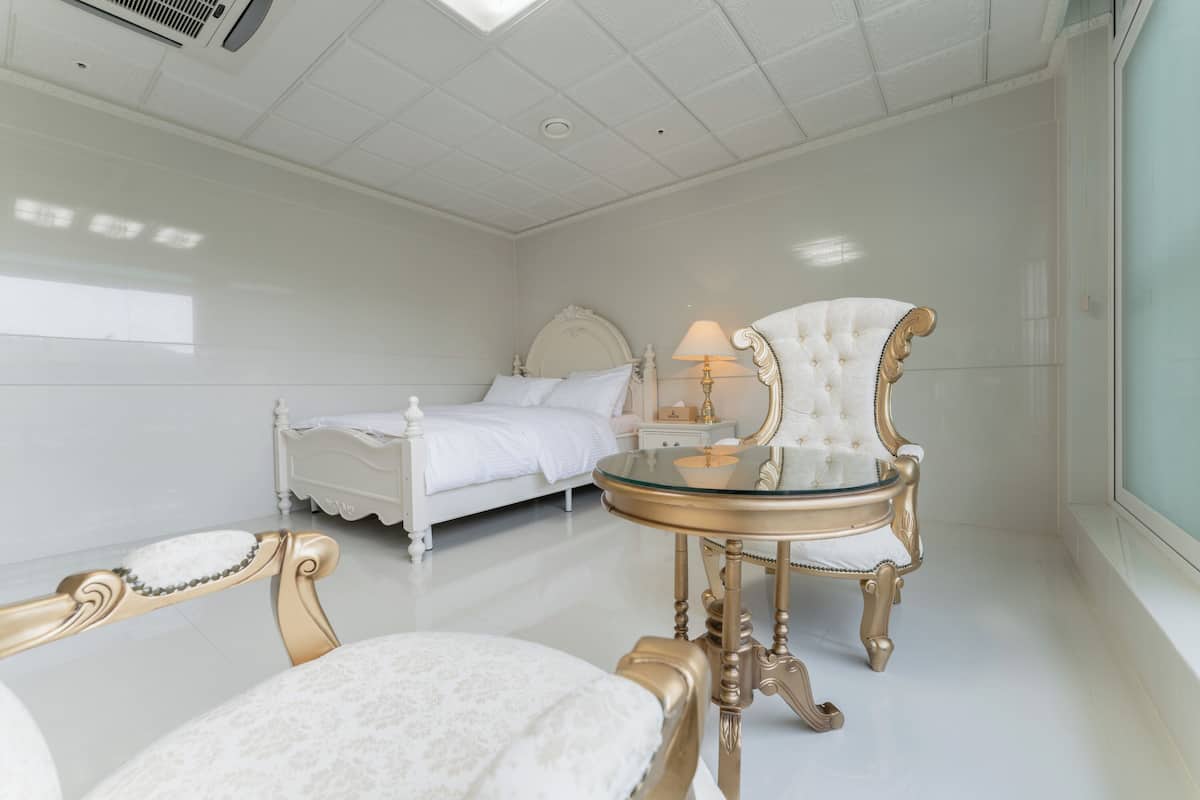 Une pièce comprenant un lit, une table en verre et une chaise aux pieds décorés.
