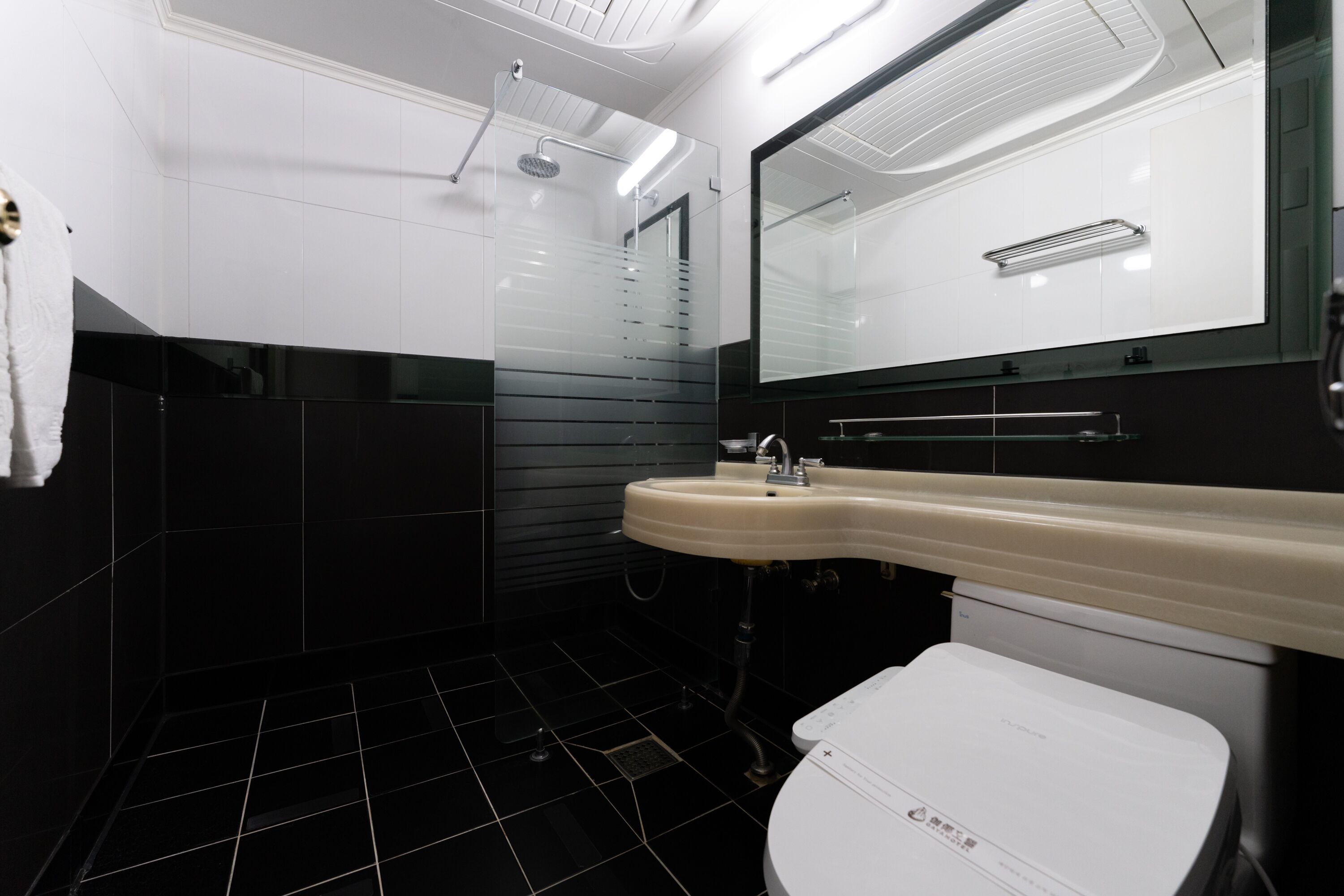 A modern bathroom with a white sink, black tiles, and a glass shower enclosure.