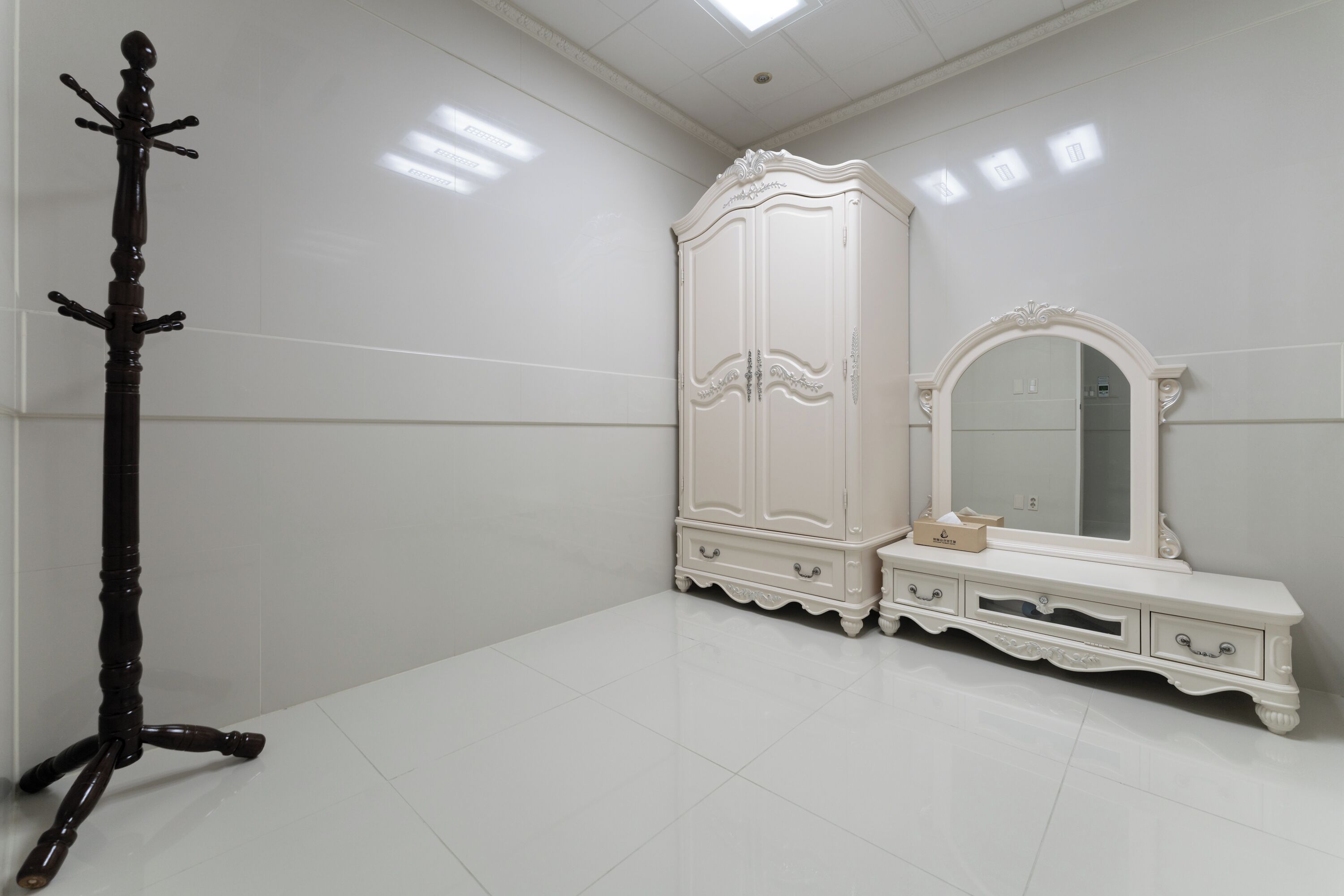 A room with a white wardrobe, a mirror, and a wooden coat rack.