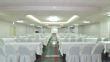 A banquet hall with rows of tables and chairs, a central aisle, and a stage at the front.