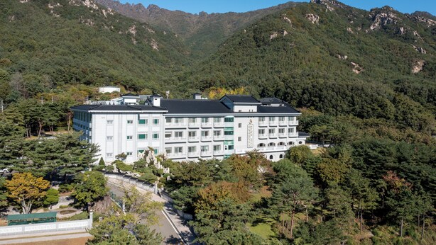 Un edificio grande con varios pisos, rodeado de bosque denso y montañas.