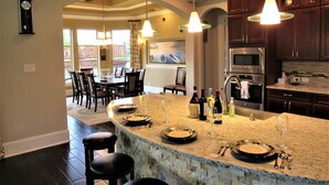 A kitchen with a large island, dark wooden cabinets, stainless steel appliances, and pendant lighting.