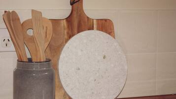 A kitchen counter with a wooden cutting board, a round white plate, and a gray vase holding wooden utensils.