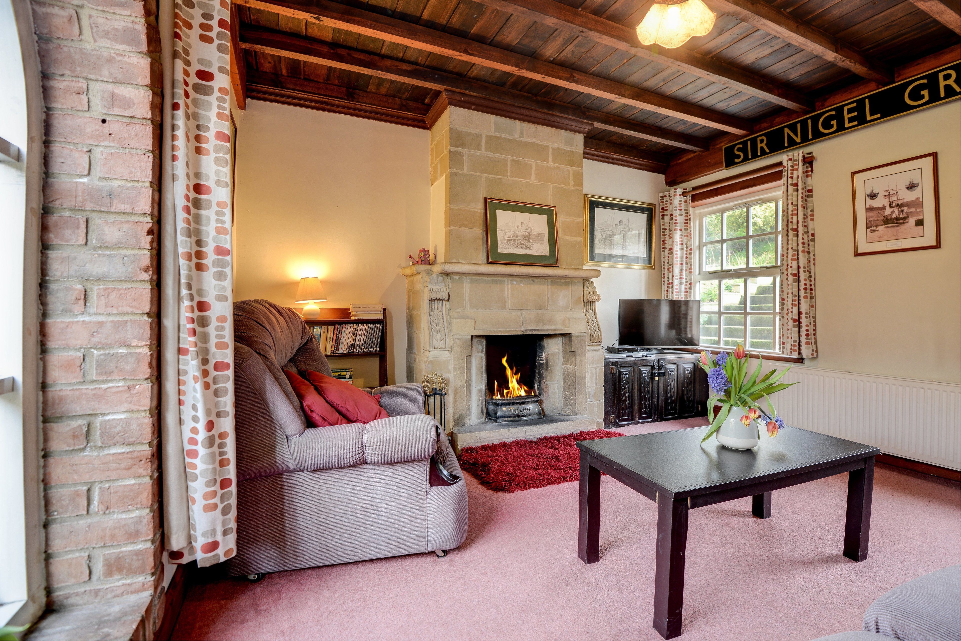 A cozy living room with a fireplace, a sofa, a TV, and a sign reading "SIR NIGEL GR".
