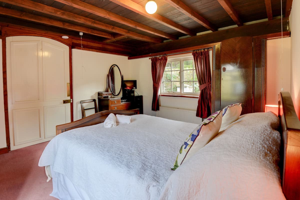 Un dormitorio con una cama grande, un tocador, un espejo y una ventana con cortinas.