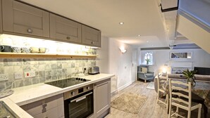 Eine moderne Küche mit integriertem Backofen, ein Essbereich mit Holztisch und -stühlen sowie ein gemütliches Wohnzimmer mit Kamin.