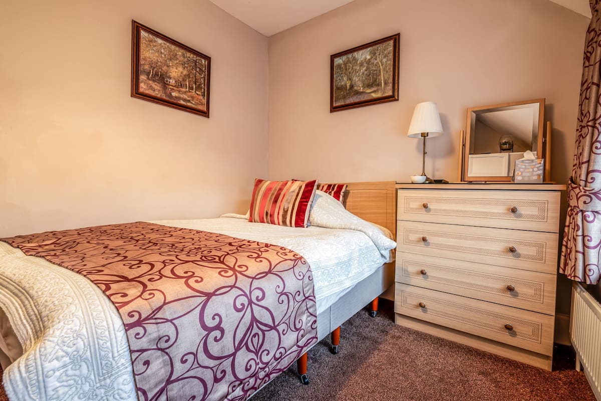 A bedroom with a bed, a dresser, a mirror, and two framed pictures on the wall.