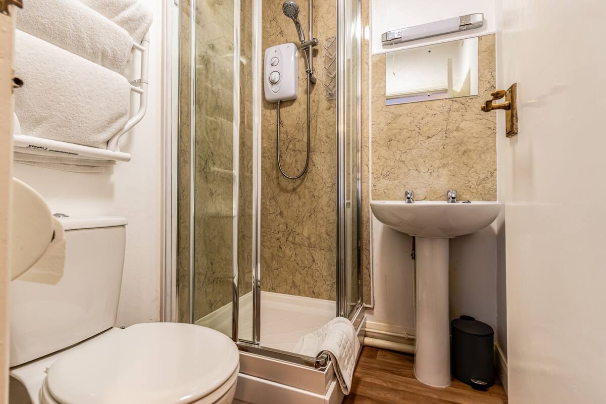 A bathroom with a glass-enclosed shower, a toilet, a sink, and a towel rack with towels.