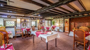Un’osteria tradizionale con travi a vista in legno, arredamento rustico e un’atmosfera accogliente. I tavoli sono apparecchiati con tovaglie rosse e sedie in vimini.