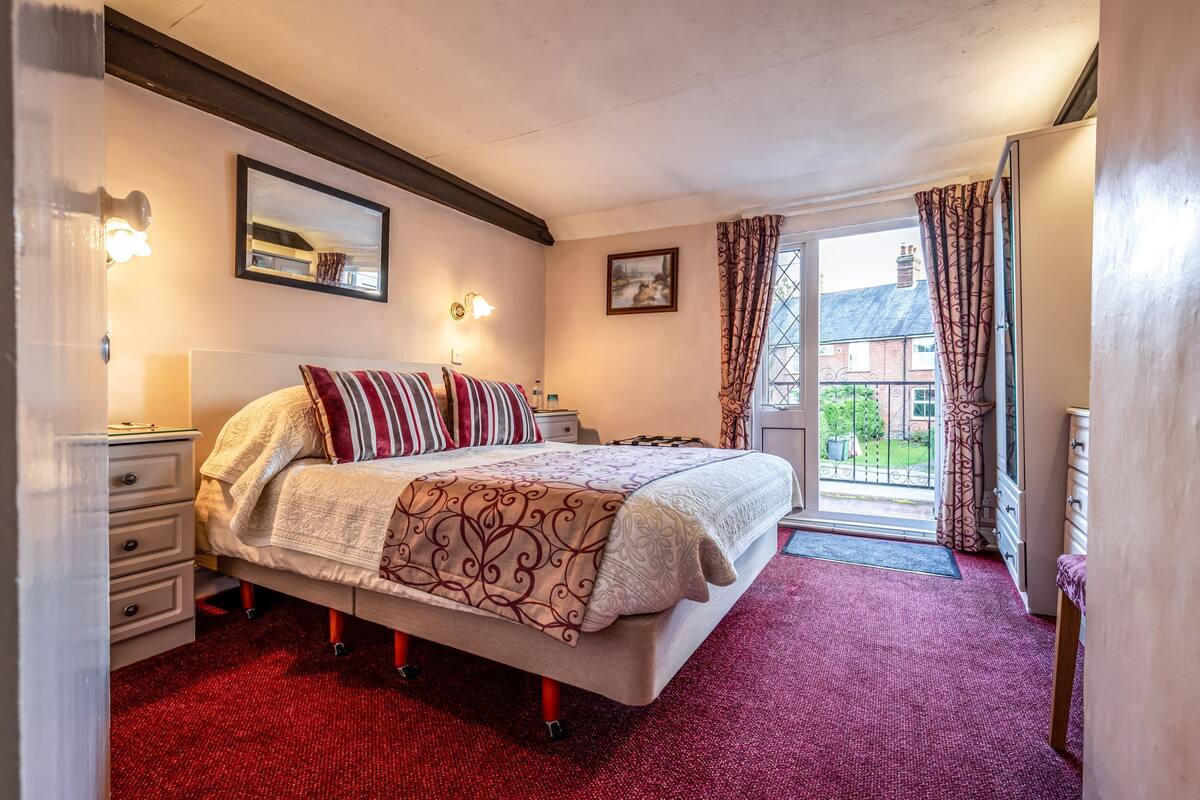 A bedroom with a large bed, a nightstand, a dresser, a window with curtains, and a view of the outside.