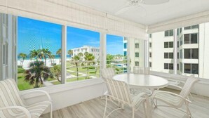 A spacious balcony with a round table and white striped chairs, overlooking a pool and palm trees. - Island House Beach Resort 14S (Siesta Key)