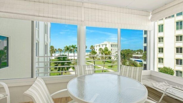 A balcony with a round table and chairs, large windows with a view of a building and palm trees. - Island House Beach Resort 14S (Siesta Key)