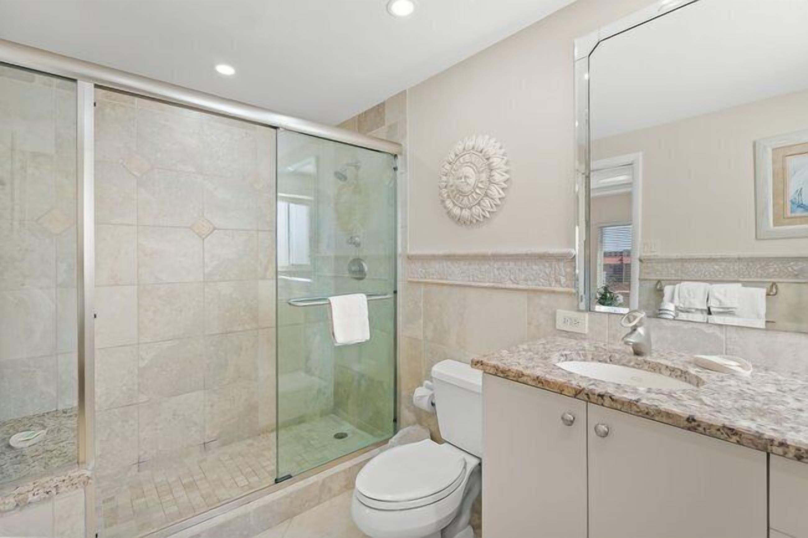 Un baño moderno con ducha de vidrio, inodoro blanco y lavamanos sobre encimera de mármol.