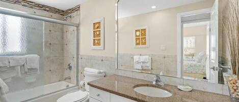 A modern bathroom with a glass shower enclosure, a white toilet, a granite countertop sink, and a large mirror.