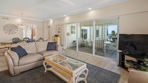 A modern living room with a sofa, coffee table, and TV. There is a sliding glass door leading to a balcony. - Island House Beach Resort 14S (Siesta Key)