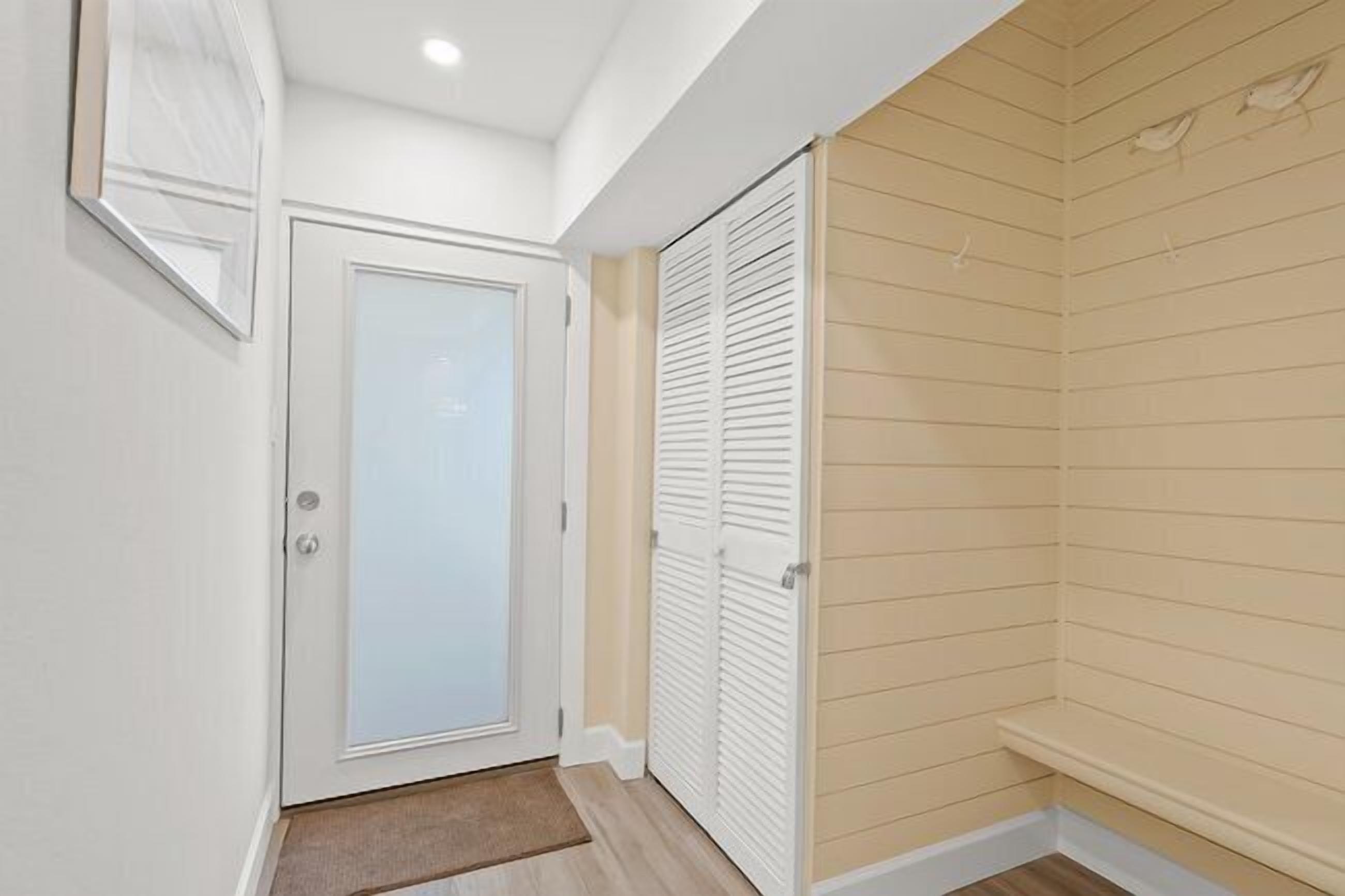 Un pasillo con una puerta blanca, un armario blanco con puertas correderas y una pared color beige con líneas horizontales.