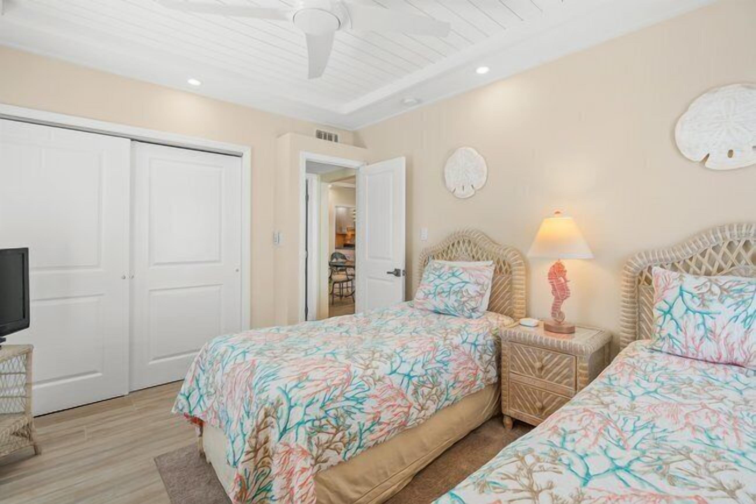 A bedroom with two beds, a television, and a door leading to another room.