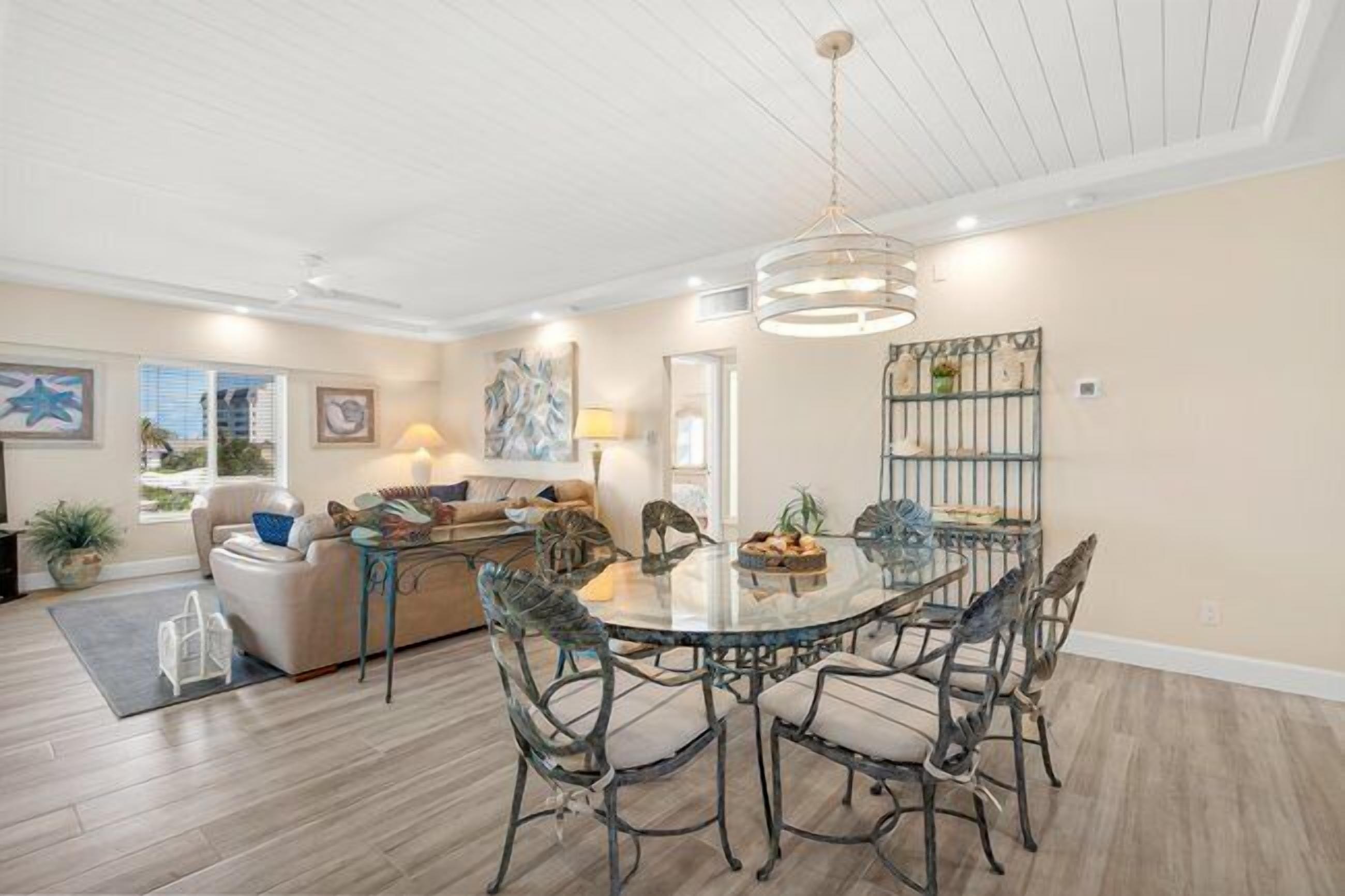A spacious living area with a round glass table and metal chairs, a sofa, and a dining table with chairs.