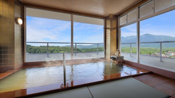 A hot spring bath with large windows offering a view of a mountainous landscape.